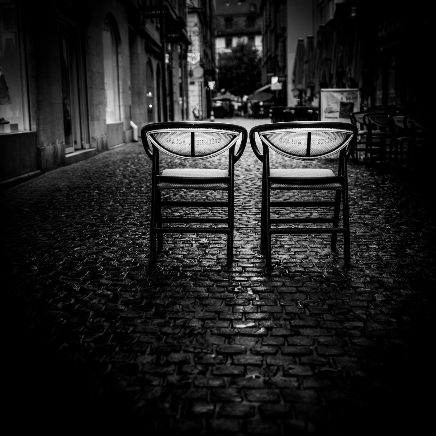 Two identical chairs, backs facing each other, in a cobbled alley at night