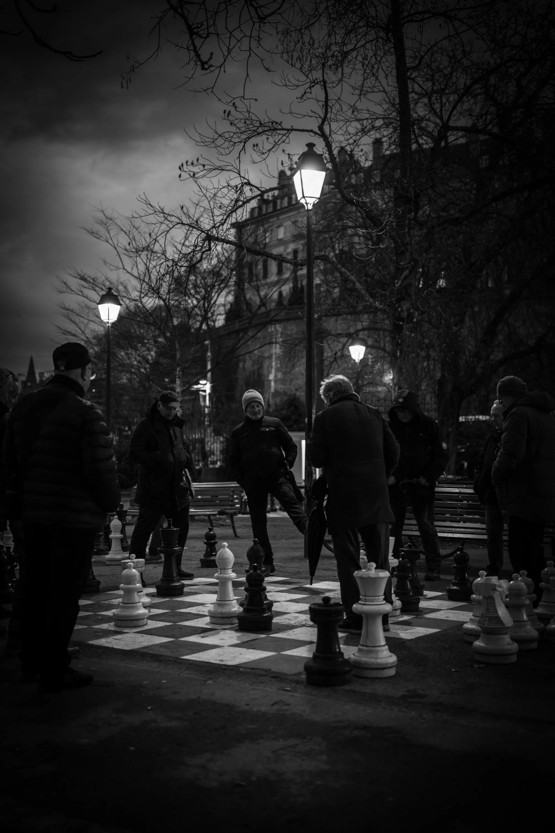 Partie d'échecs géante en plein air, la nuit, sous les réverbères