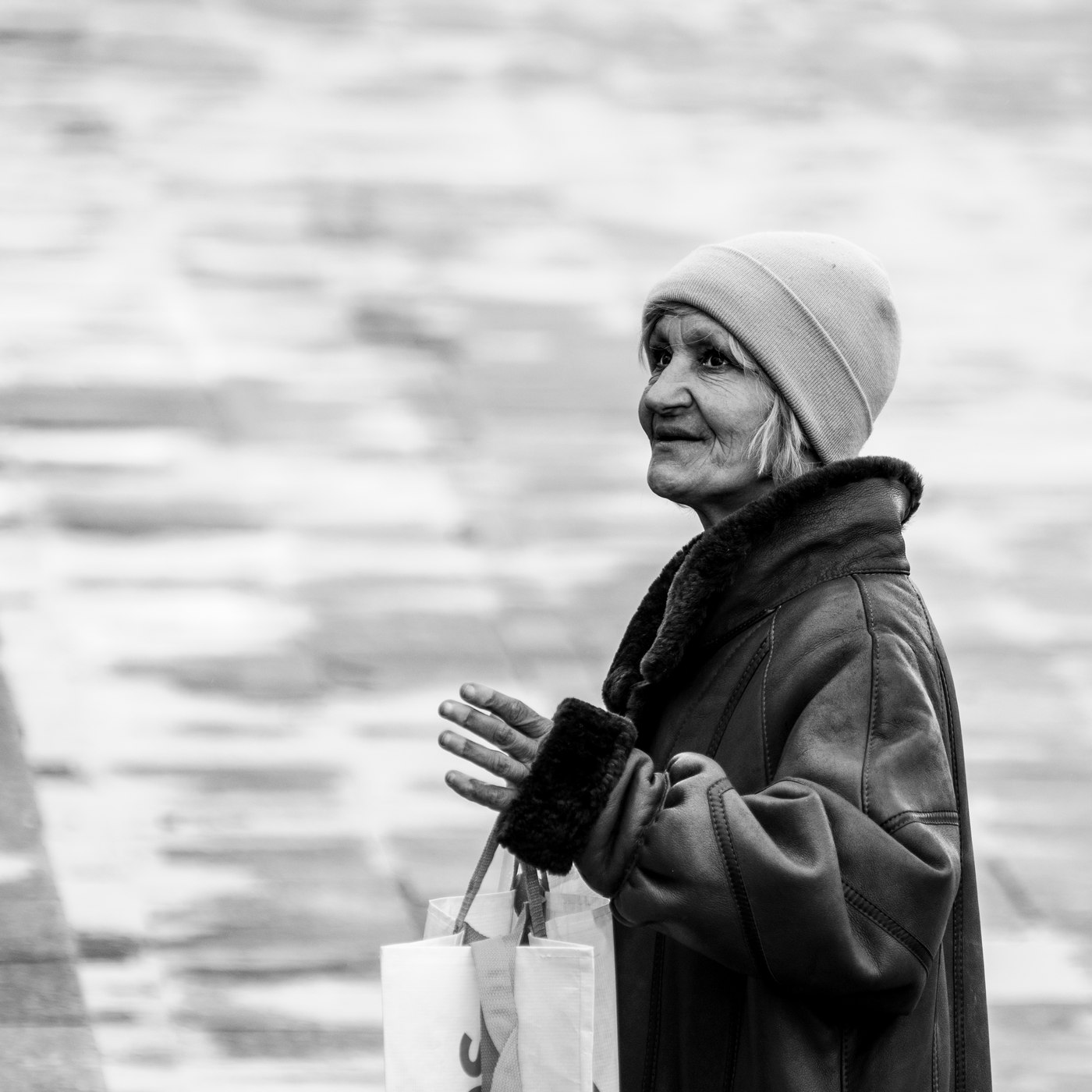 Portrait of a woman in the street, beanie and coat, hands clasped