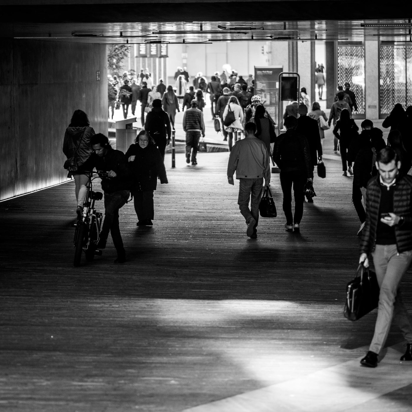 Une foule dense marche dans un passage souterrain, silhouettes à contre-jour